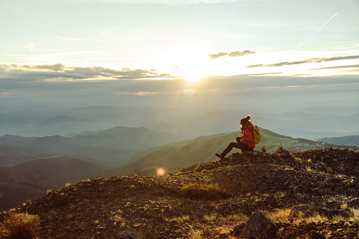 Female hiker sitting on a mountain peak looking at the view at sunset
