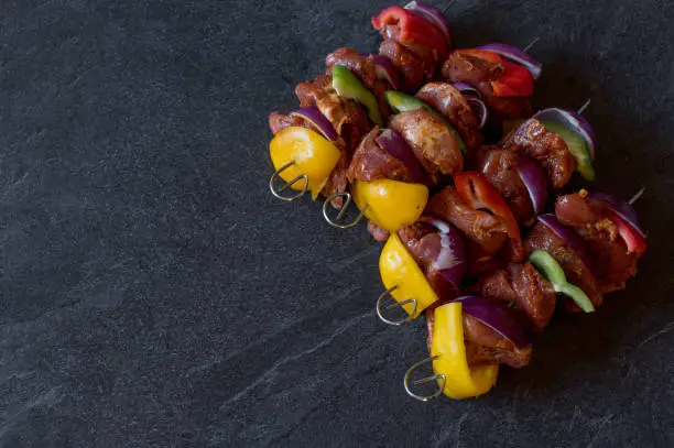 Raw shashlik skewers with red, green and yellow bell peppers and onions isolated on dark background from above. Side view with copy space