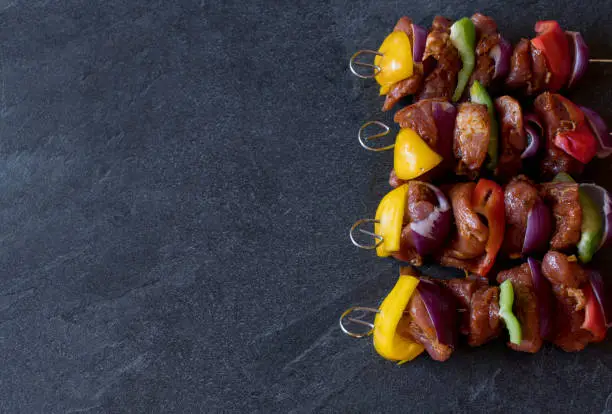 Shish kebab skewers with red, green and yellow bell peppers, red onions and marinated pork tenderloin isolated on dark background. Side view with copy space