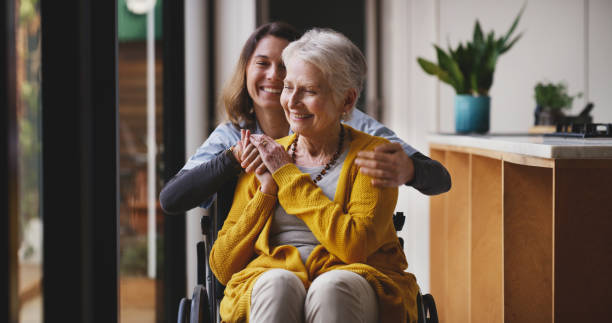 Nurse, disability and care with a senior woman in a wheelchair during a visit from a caregiver in a retirement home. Insurance, medical or healthcare with a female carer and mature patient in a house stock photo
