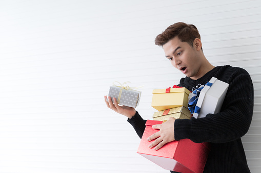 Portrait of a exciting Asian young man holding many gifts box on wall white background