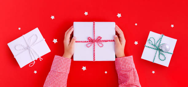 istock Christmas banner gift box in children's hands on a red background, presenting a gift 1441687040