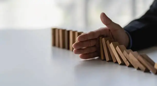 Photo of Businessman stops her hand blocking or falling dominoes Financial business and risk management Businessman prevents wooden blocks from falling with his hands