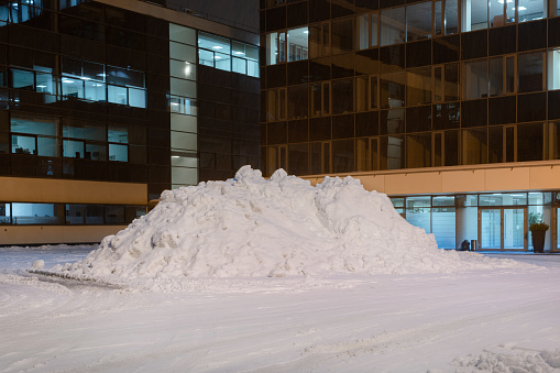 Pile of white snow in front of a office building. Huge heap of white street snow in the city at night.
