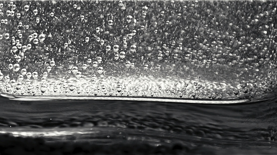 Close-up of small bubbles floating in the glass filled with sparkling water on the dark background. Stock footage. Monochrome