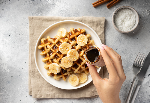 female hand pouring date syrup on banana oatmeal waffles. Healthy food concept. top view