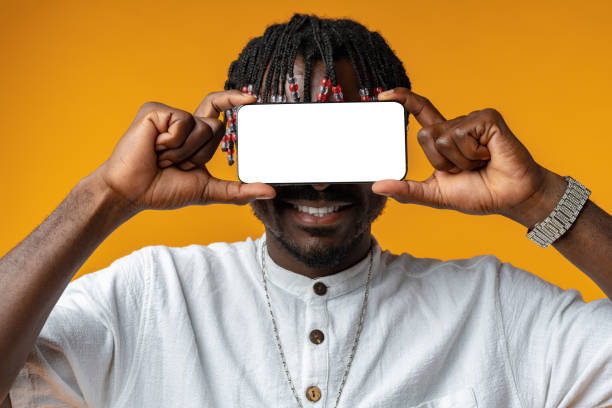 istock Excited young african man holding smartphone with white blank screen in hand on yellow studio background 1441691034