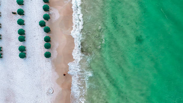 Top Down Drone Image of Tide Breaking on Beach in Destin, Florida Tide breaking on Destin Beach. Emerald green waters in the morning as waves crash on Destin Beach. Fish swimming in low tide. Beach chairs and umbrellas set up in the morning for tourists and vacationers to relax on a Florida day. florida beach above stock pictures, royalty-free photos & images