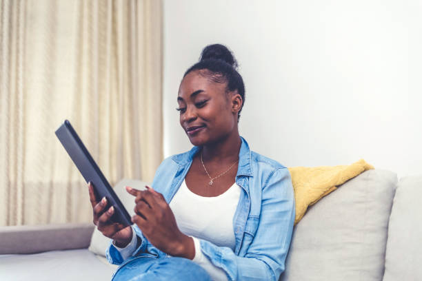 istock Working from home. A young woman using a digital tablet to read/watch something. Smiling African American woman busy browsing tablet. 1441694287