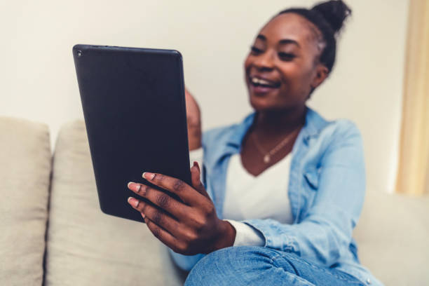 istock Working from home. A young woman using a digital tablet to read/watch something. Smiling African American woman busy browsing tablet. 1441694423