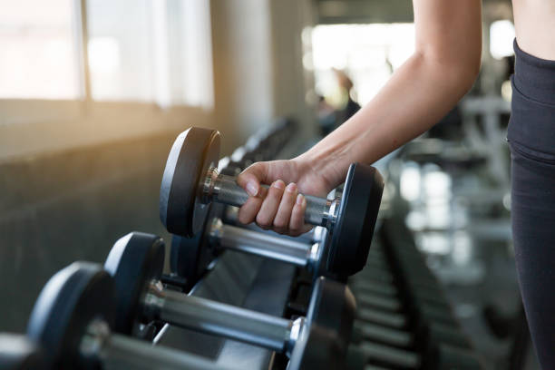 mano della donna atleta che tiene il manubrio dal rack in palestra. esercizio femminile di fitness muscolare con manubri nello sport di palestra. concetto per l'esercizio del fitness e l'allenamento di stile di vita sano - weightlifting foto e immagini stock