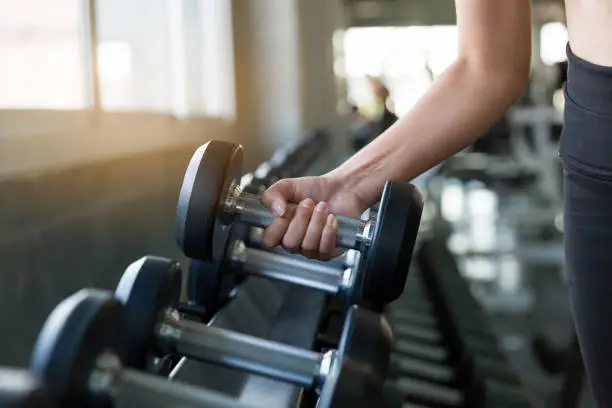 Photo of Hand of athlete woman holding dumbbell from the rack in the gym. Muscular fitness female exercise with dumbbell in the gym sport. Concept for exercising fitness and healthy lifestyle workout