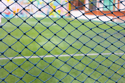 Selective focus shot behind goal net with blurred background of greeny grass or lawn of soccer field in summer time shows concept of sport and recreation activity and also teamwork for success.