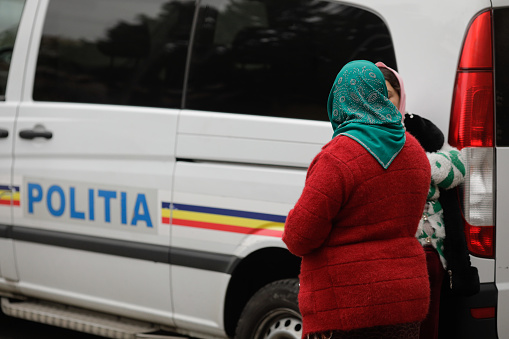 Bucharest, Romania - November 15, 2022: Two Roma women stand next to a Romanian Police van.