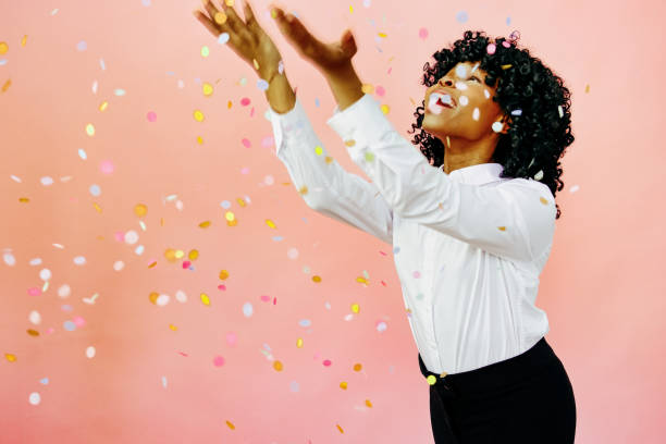 special occasion portrait of a happy woman with arms out, smiling at confetti falling - businesswoman black african descent studio shot imagens e fotografias de stock