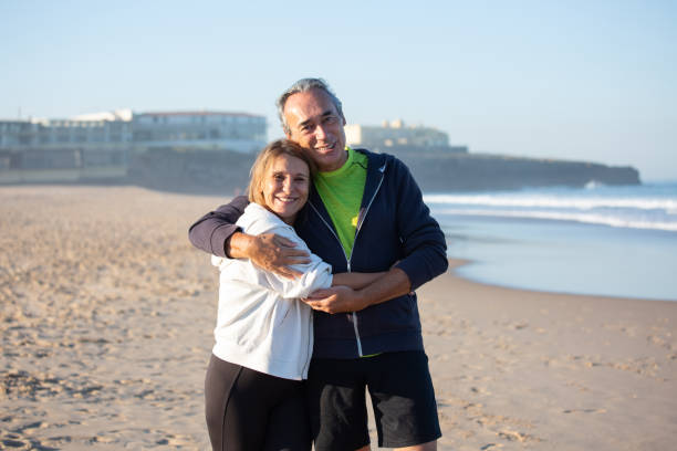istock Senior man and woman hugging on sandy beach, looking at camera 1441703203