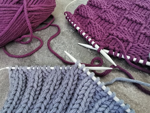 Gray and purple pieces of knitting on gray background. Knitted patterns and textures close up. Needlework hobbies.