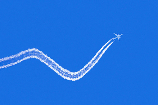 Looking up at a commercial passenger jet with up and down condensation trails against a clear blue sky, concept the highs and lows of air travel.