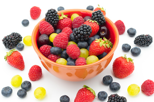 Ceramic brown bowl full with an assortment of different forest fruits (blueberries, raspberries, blackberries and strawberries), cherries and grapes.  White background.