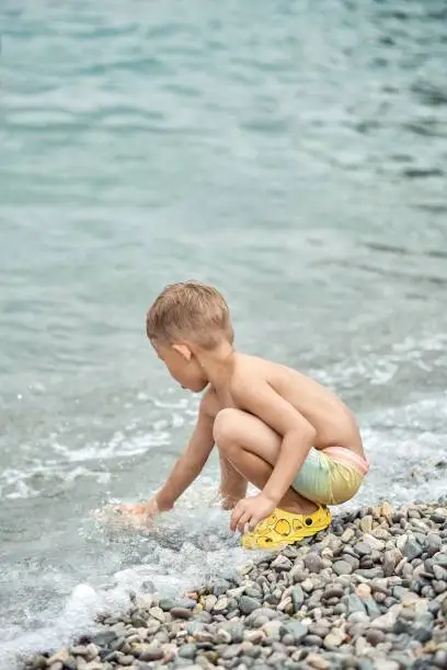 Photo of Preschooler boy plays on beach of sea catching waves