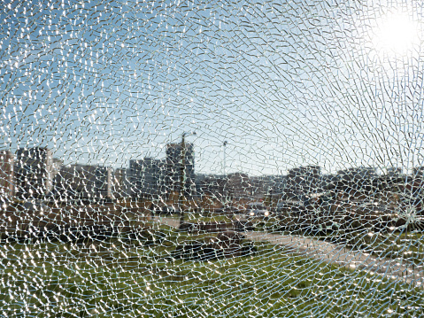 View through the broken glass on the blue sky, the sun and the city in the distance. Background of broken glass in small cracks on a sunny day. Concept background and wallpaper..