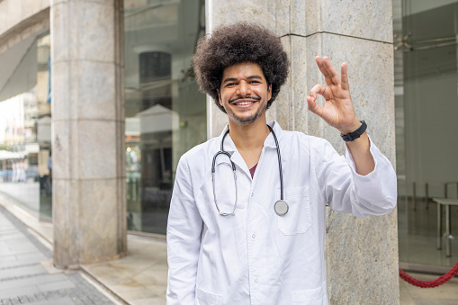 Doctor smiling when standing in front of the hospital and gesturing ok sign