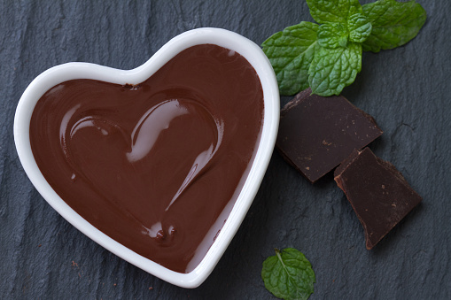 Delicious chocolate mousse with mint in heart-shaped bowl on dark background concept