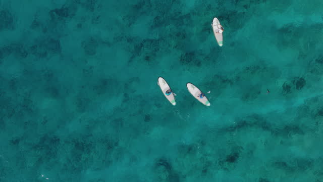 Aerial view of three people having fun on a stand up paddle board paddling around a tropical Island at sunset