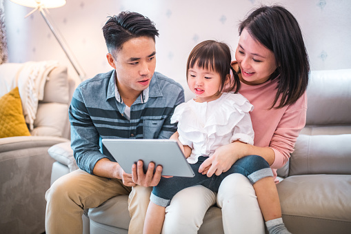 Chinese father and mother using a digital tablet with their little daughter. They are enjoying a peaceful weekend at home while using wireless technology.