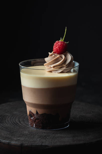 istock Layered dessert Trifles decorated with raspberry.  Sponge biscuit and three chocolate mousse layers. Chocolate souffle trifle cake in individual disposable transparent cups. Black background 1441719021