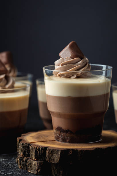 istock Layered dessert Trifles in a transparent glass.  Sponge biscuit and three chocolate mousse layers. Chocolate souffle trifle cake in individual disposable transparent cups. Black background 1441719040