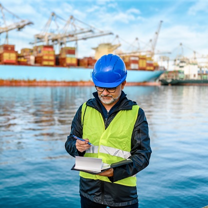 Shot of man reading paperwork while standing on a large commercial dock