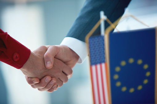 Officials of foreign countries shaking hands, USA and EU flags up front
