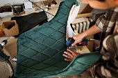 Young upholstery worker applying fabric on a chair with a pneumatic stapler in the workshop