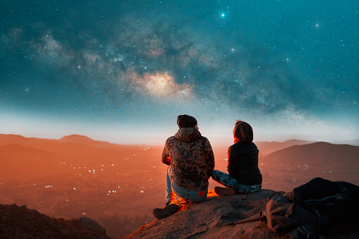 latin couple sitting on top of a hill at night with milky way in the background enjoying the landscape in Valle del Elqui
