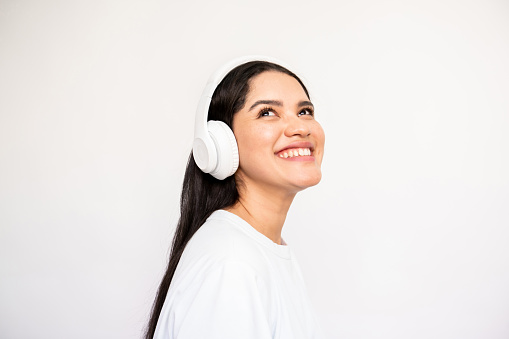 Portrait of cheerful young woman wearing headphones. Caucasian lady wearing white T-shirt listening to music and smiling. Music and leisure concept
