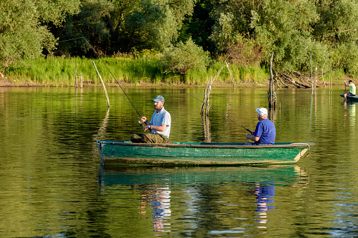 Novi Sad, Serbia - July 06, 2022: Danube island (Šodroš) near Novi Sad, Serbia. Fishermans sitting in boat and holding fishing rod.