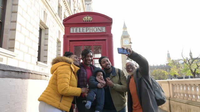 Smiling tourists taking selfie next to red telephone box
