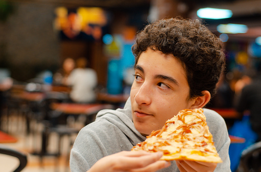 Teenage boy eating slice of pizza looking away and copy space