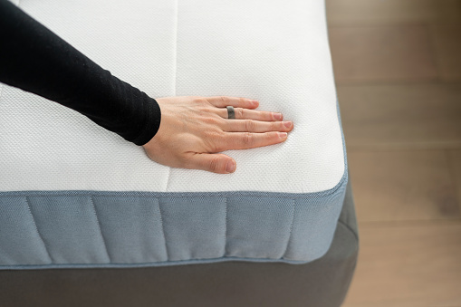 Buyer checks the quality of the memory foam mattress. High angle view of woman hand presses at topper on bed, choosing product for bedroom in furniture store. Health care, healthy sleeping concepts