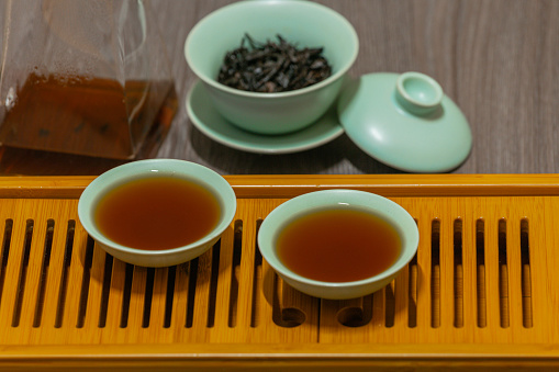 Brewing Chinese tea in a ceramic gaiwan during a tea ceremony close-up. Gaiwan and other tea accessories for the ceremony on a bamboo tea table.
