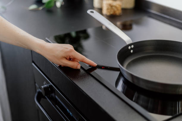 woman turn on induction stove at kitchen, cropped shot stock photo