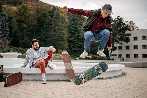 Young man supports a friend who performs tricks with a skateboard