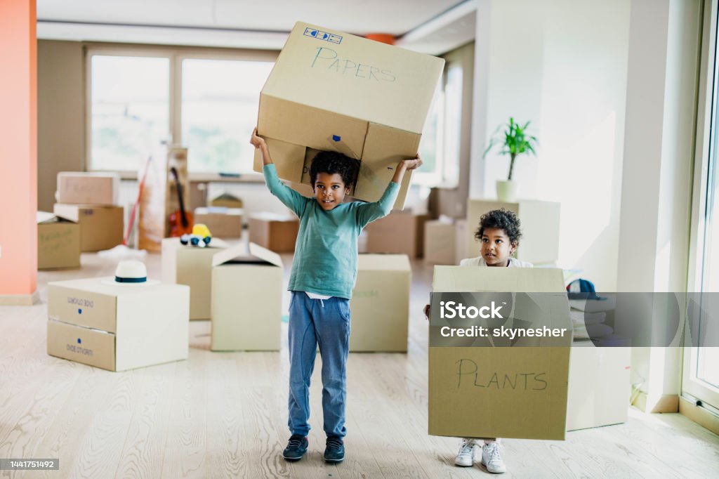 Small black kids carrying cardboard boxes in their new home. Little African American kids carrying carton boxes at their new apartment. African Ethnicity Stock Photo