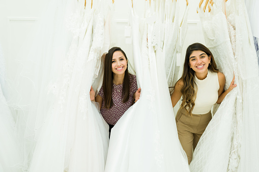 Cheerful young women looking for the perfect wedding dress at the bridal store and having fun