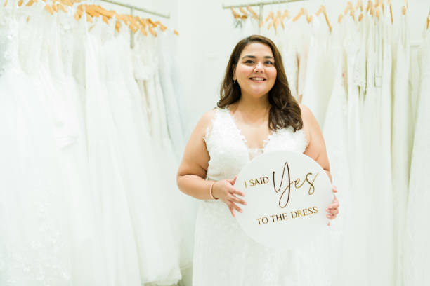 Excited overweight woman smiling after buying her wedding gown Beautiful latin chubby woman saying yes to dress while shopping for a wedding dress at the bridal store bridal boutique stock pictures, royalty-free photos & images
