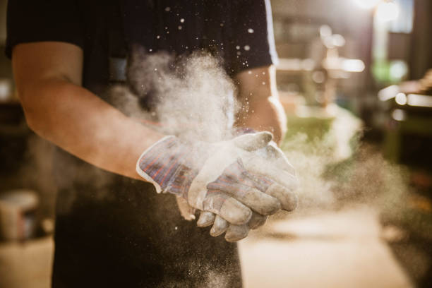 Close up of unrecognizable manual worker cleaning sawdust from his protective gloves in a workshop.