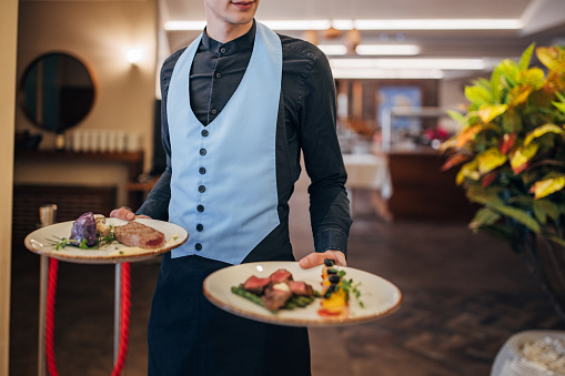 Waiter is carrying plates with delicious meals for the luxury restaurant guests.