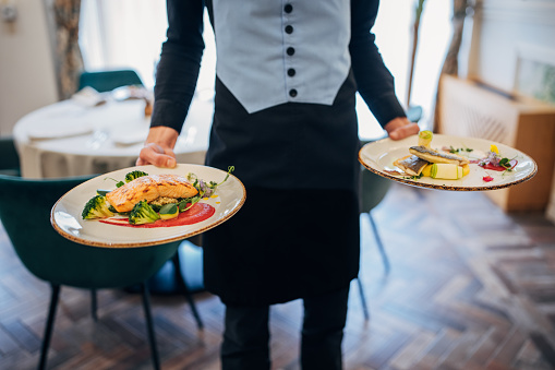 Waiter is carrying plates with delicious meals for the luxury restaurant guests.