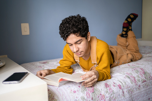 Portrait of young gay man reading a book in bed